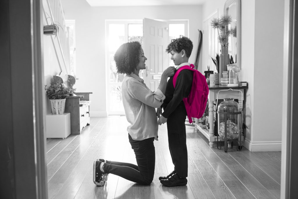 Image shows mum kneeling down to fix son's school shirt as he prepares to go to school. The young boy has a backpack on which is coloured pink to match Fraser Dawbarns' colour scheme and both the mother and son are in a hallway in a house.