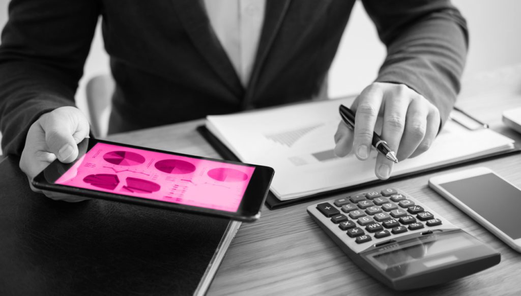 Image shows businessman at desk using digital tablet to analyse financial statistics chart. There is a calculator on the desk.