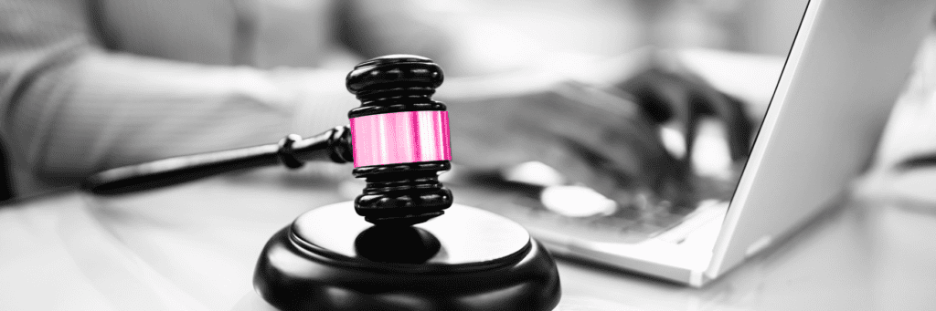 A gavel with a pink band and a person working from a computer behind