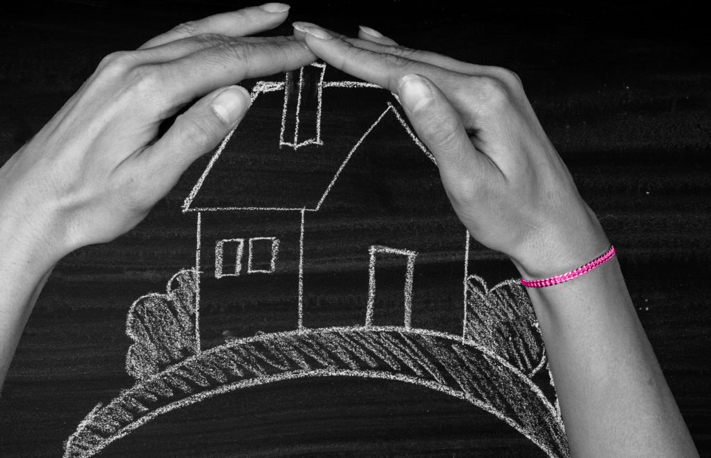 Image shows house drawn in chalk on blackboard covered by pair of hands so to show it is protected.