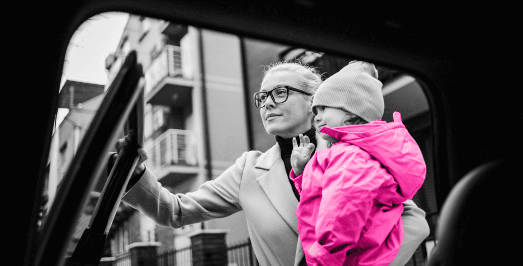 lady carrying a child in a pink jacket after getting them out of the car
